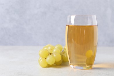 Photo of Tasty grape juice in glass and berries on light table, closeup. Space for text