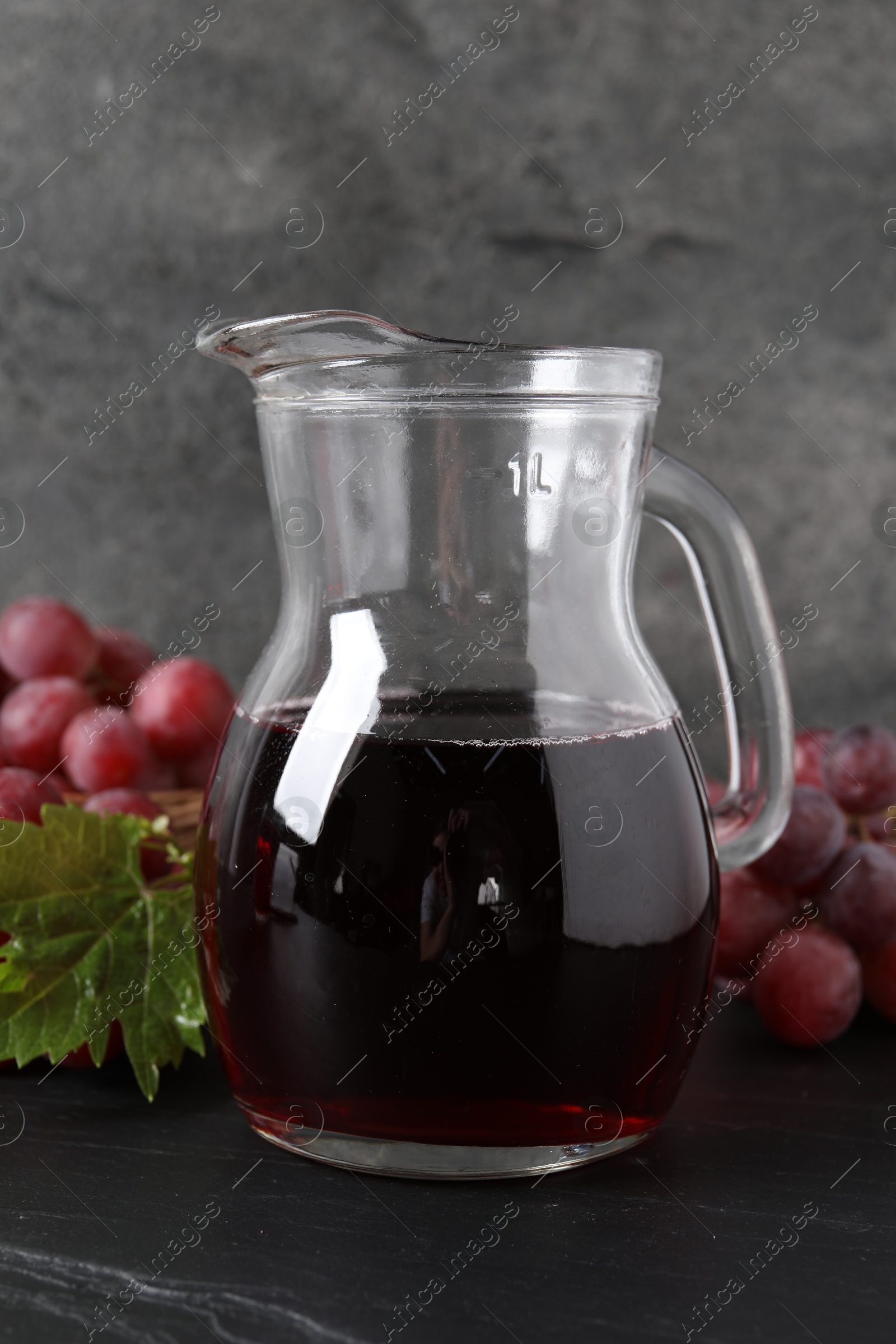 Photo of Tasty grape juice in jar, leaf and berries on dark textured table