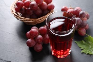 Photo of Tasty grape juice in glass and berries on dark textured table, closeup