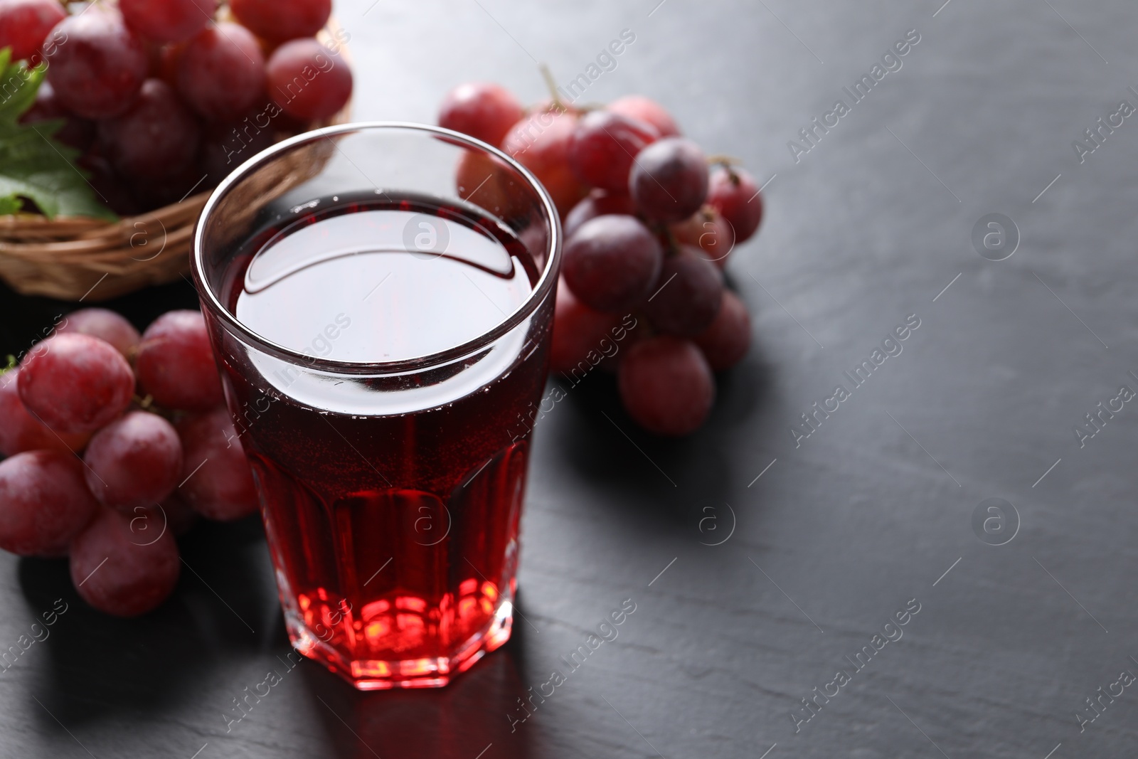 Photo of Tasty grape juice in glass and berries on dark textured table, closeup. Space for text