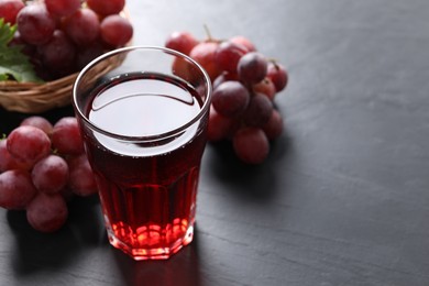 Tasty grape juice in glass and berries on dark textured table, closeup. Space for text