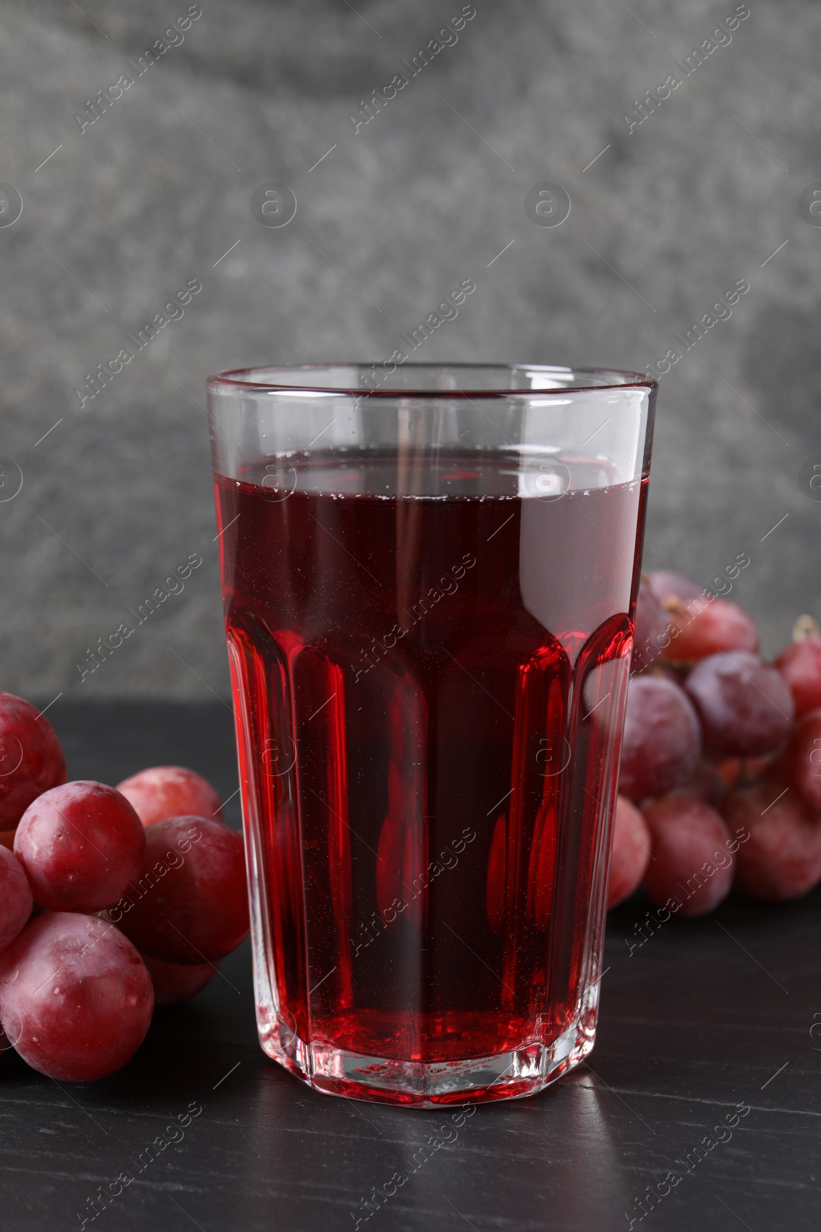 Photo of Tasty grape juice in glass and berries on dark textured table, closeup