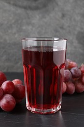 Photo of Tasty grape juice in glass and berries on dark textured table, closeup