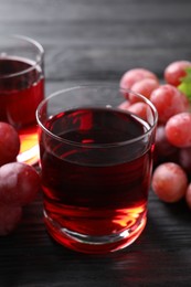 Photo of Tasty grape juice in glass and berries on black wooden table, closeup