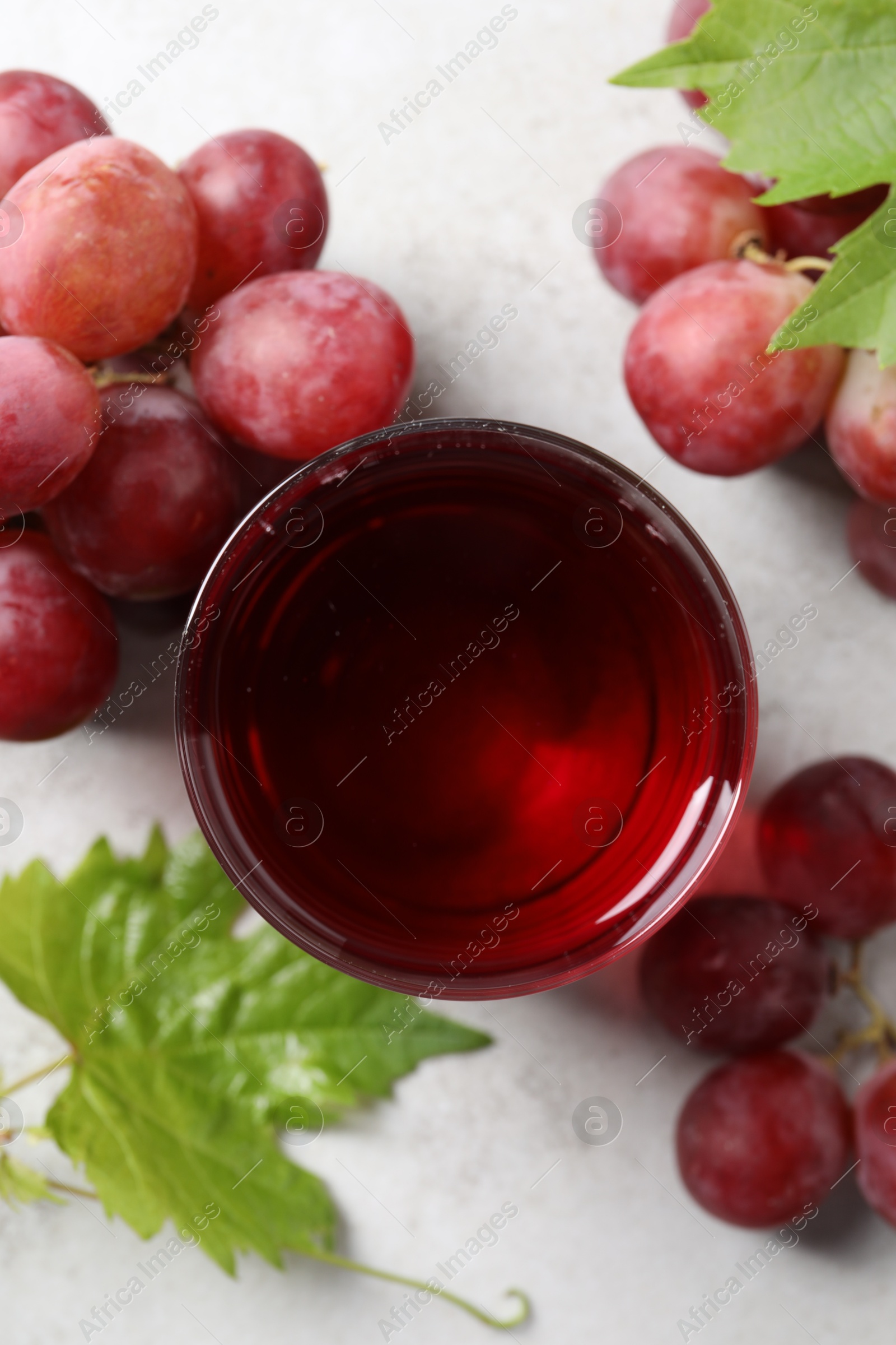 Photo of Tasty grape juice in glass, leaves and berries on light table, flat lay