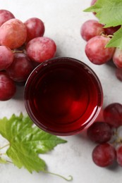 Photo of Tasty grape juice in glass, leaves and berries on light table, flat lay