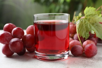 Tasty grape juice in glass, leaf and berries on light textured table against blurred green background, closeup