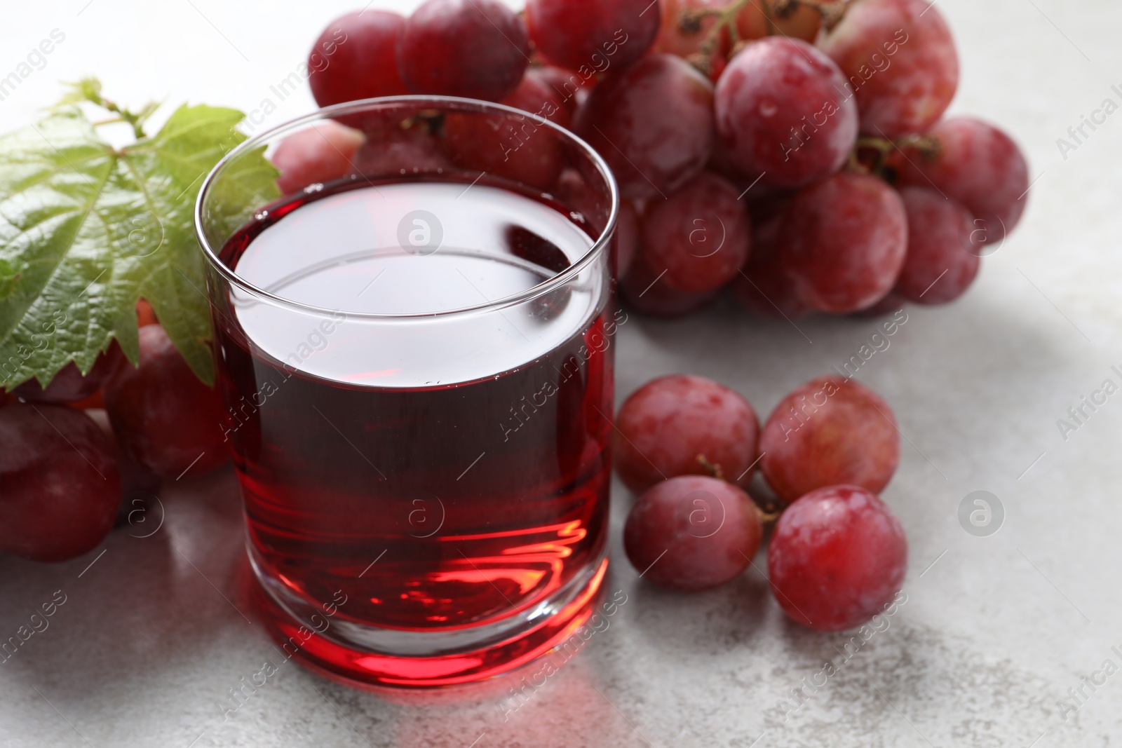 Photo of Tasty grape juice in glass, leaf and berries on light textured table, closeup