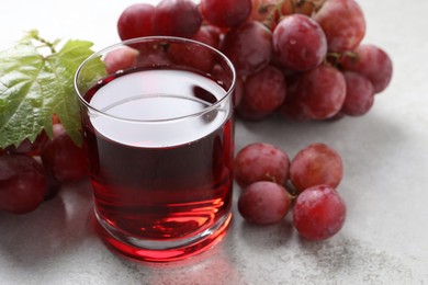 Photo of Tasty grape juice in glass, leaf and berries on light textured table, closeup