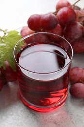 Photo of Tasty grape juice in glass, leaf and berries on light textured table, closeup