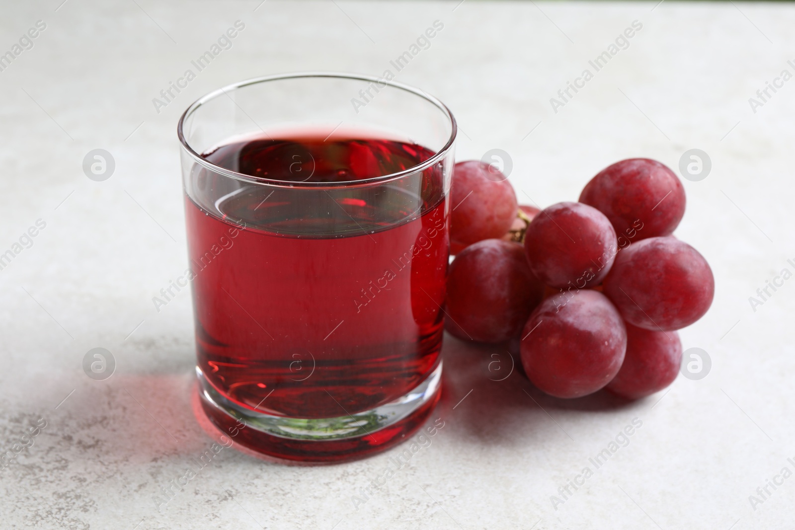 Photo of Tasty grape juice in glass and berries on light textured table, closeup