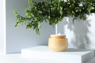 Facial cream in jar and floral decor on white table