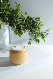 Facial cream in jar and floral decor on white table