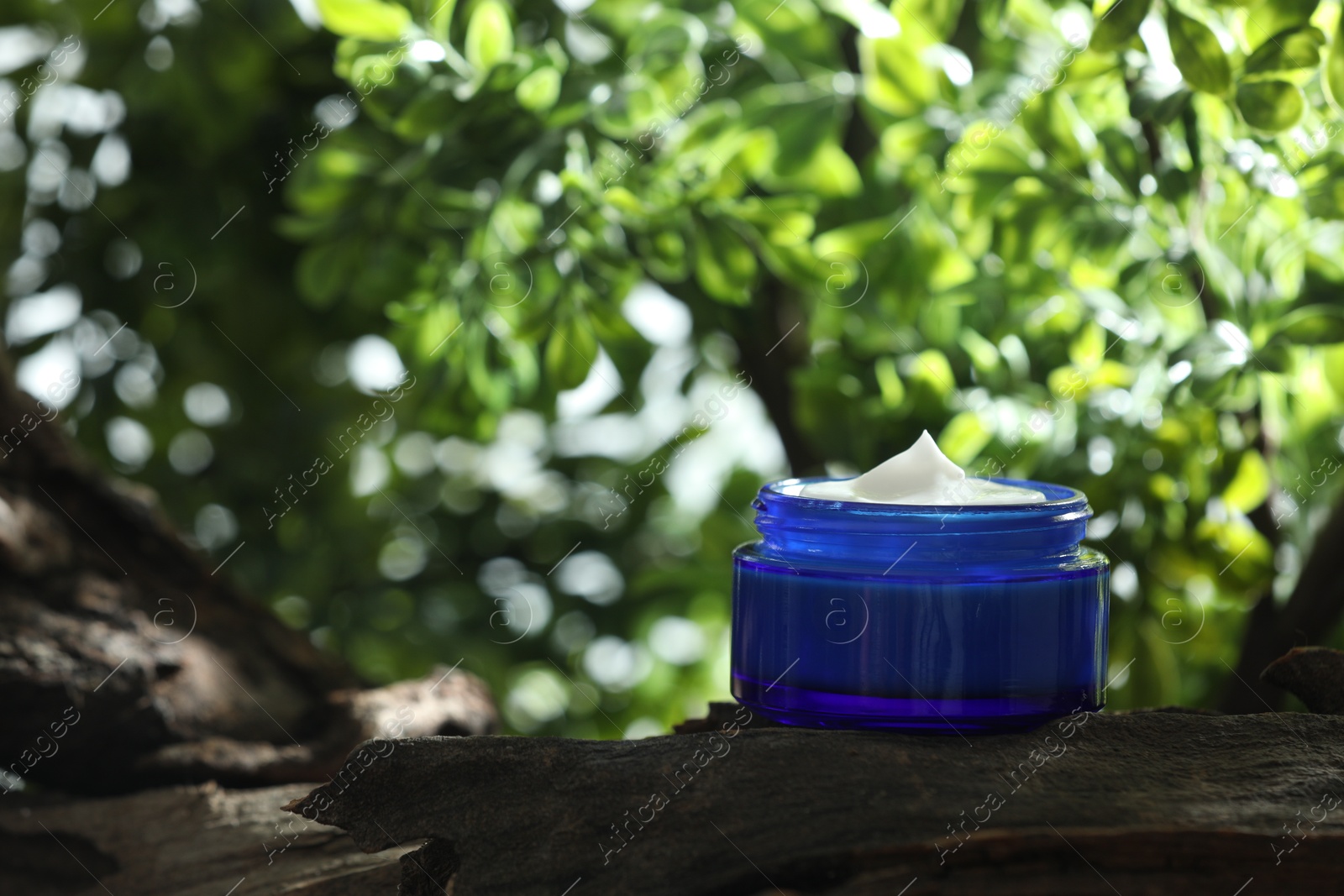 Photo of Stylish presentation of facial cream in jar outdoors, closeup. Space for text