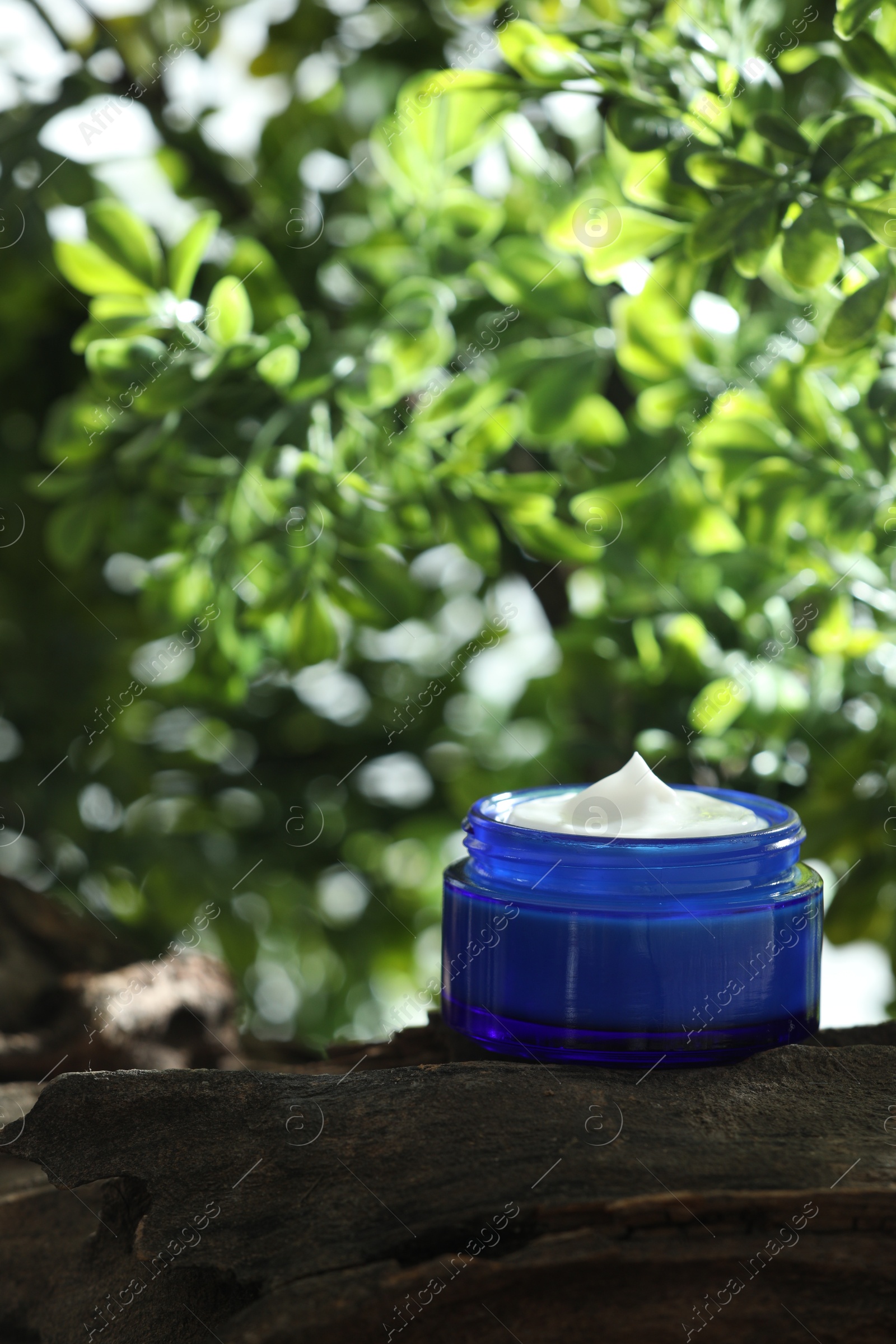 Photo of Stylish presentation of facial cream in jar outdoors, closeup. Space for text