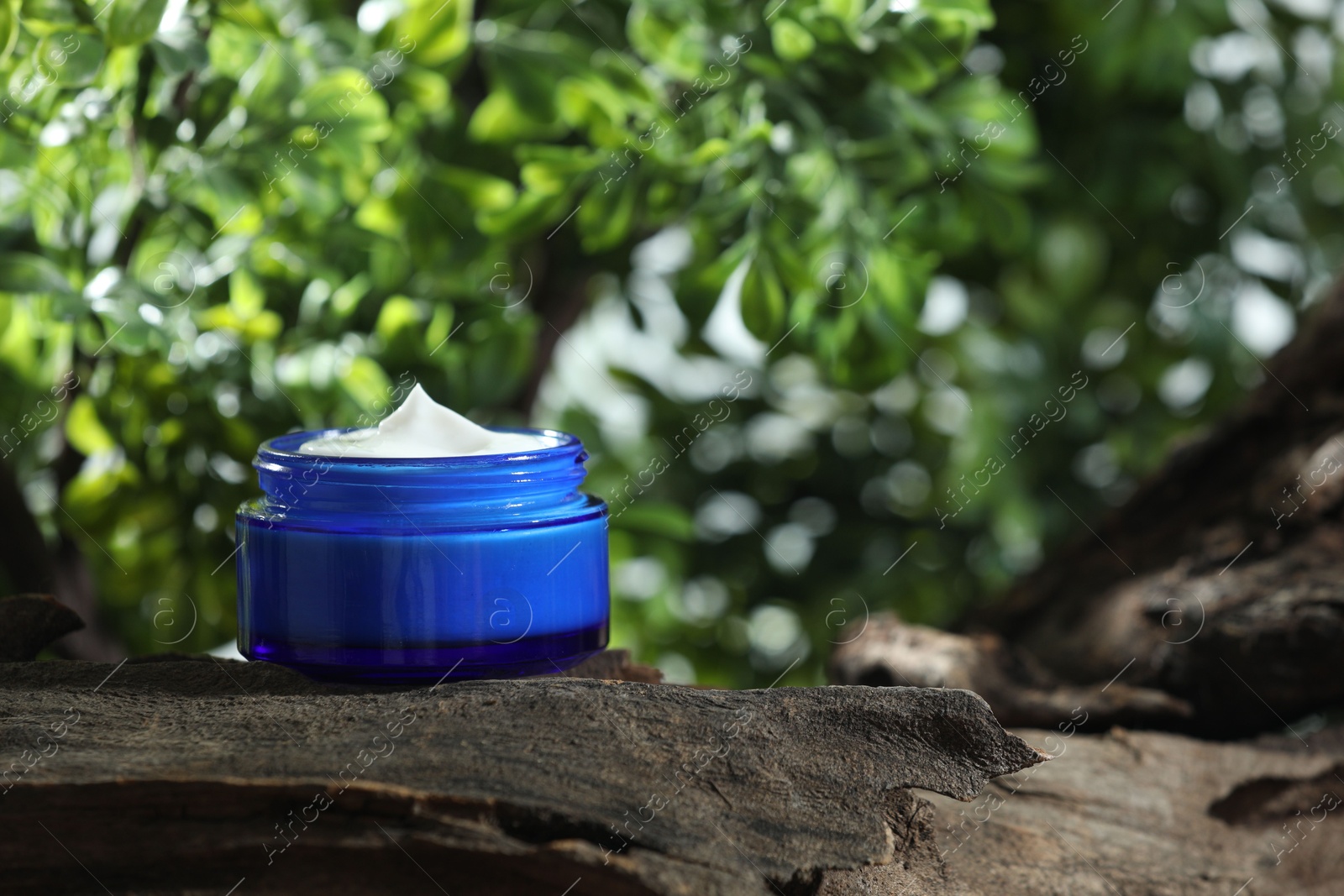 Photo of Stylish presentation of facial cream in jar outdoors, closeup. Space for text