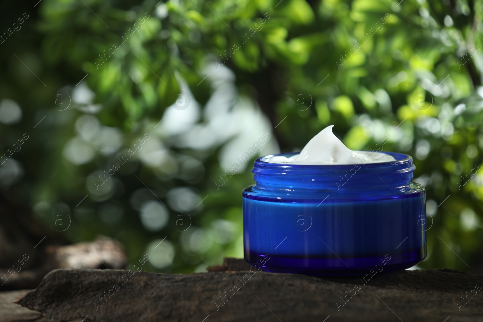 Photo of Stylish presentation of facial cream in jar outdoors, closeup. Space for text