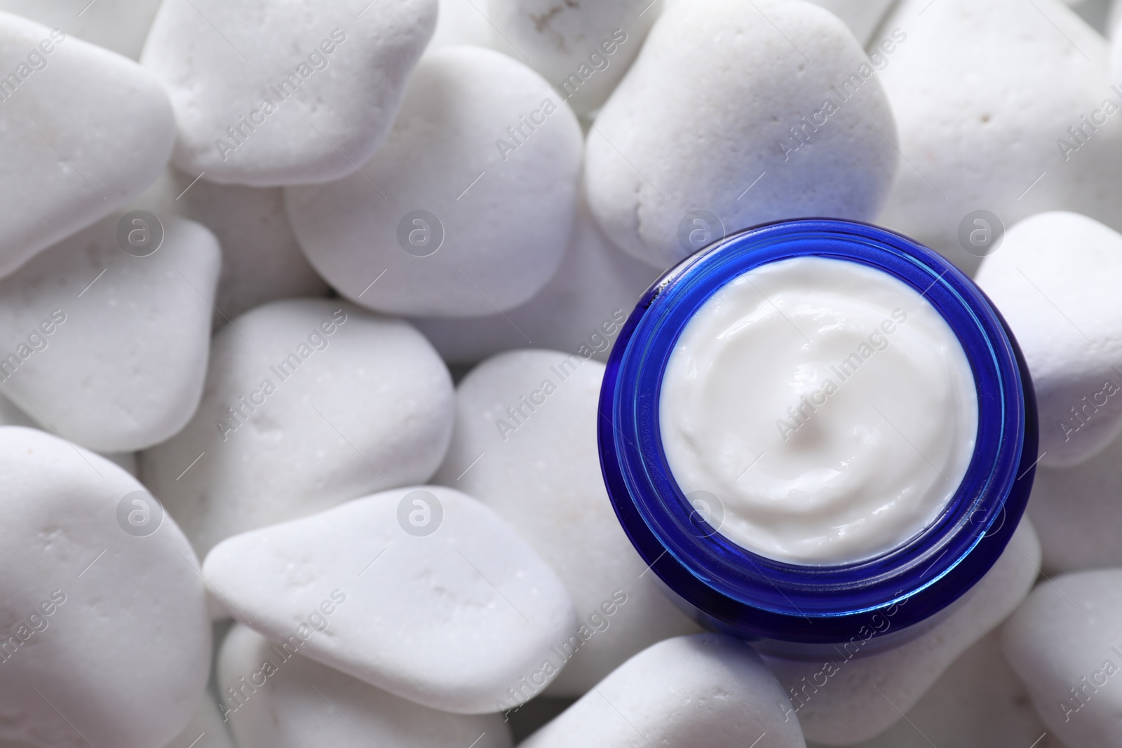 Photo of Face cream in jar on white stones, top view. Space for text