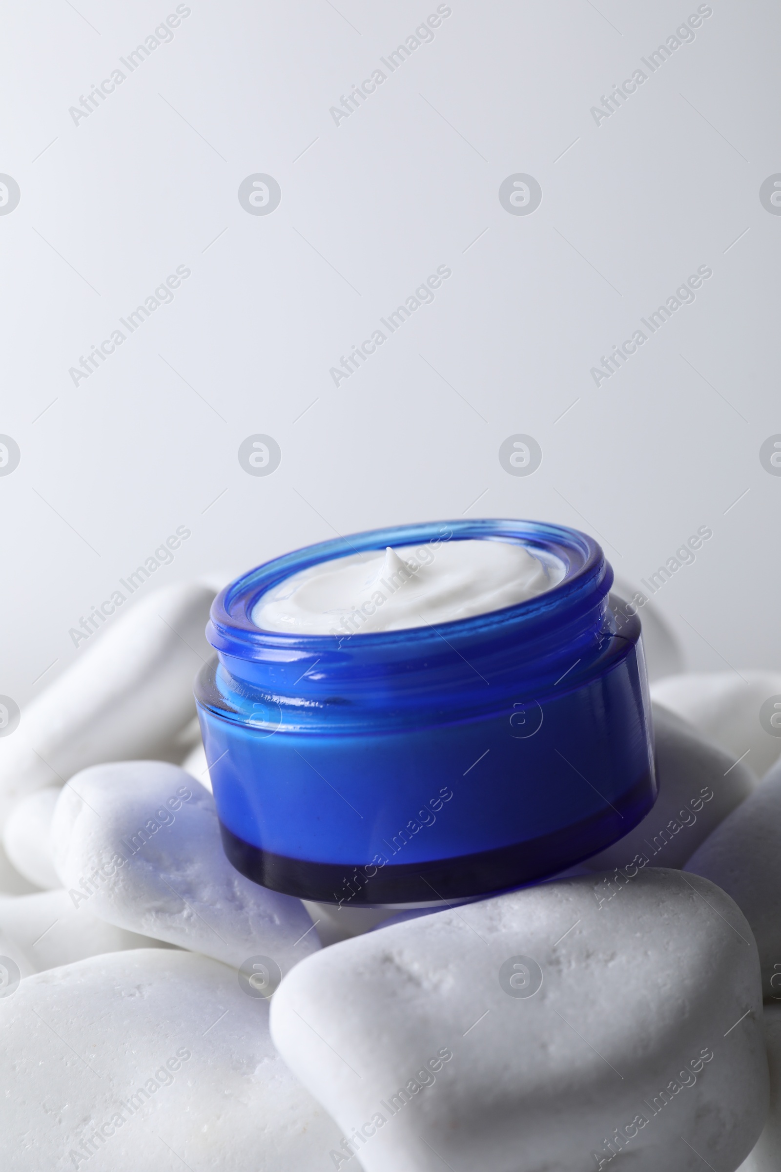 Photo of Face cream in jar on stones against light background, closeup