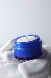 Photo of Face cream in jar on stones against light background, closeup