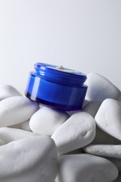 Photo of Face cream in jar on stones against light background