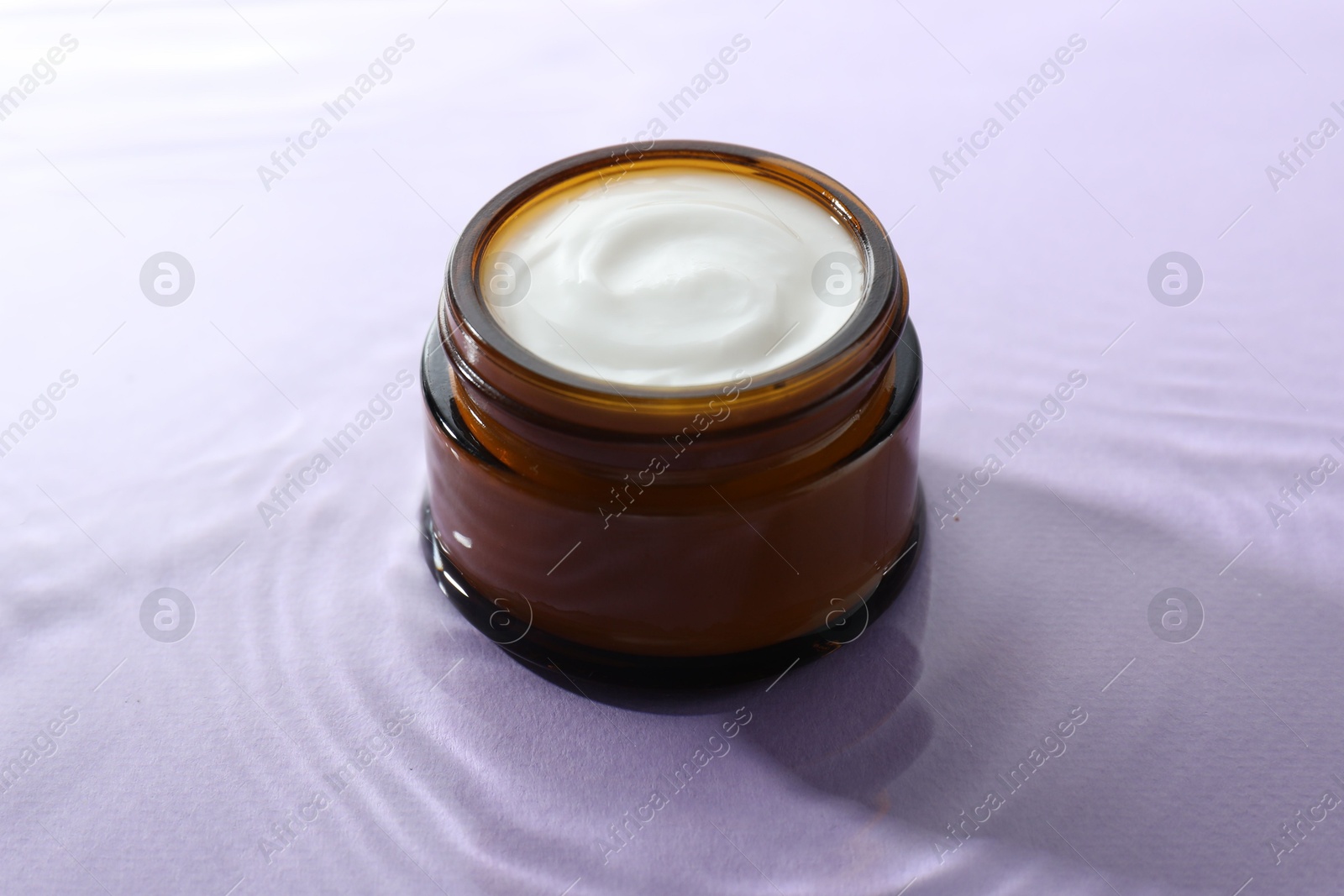 Photo of Jar with face cream in water on light violet background