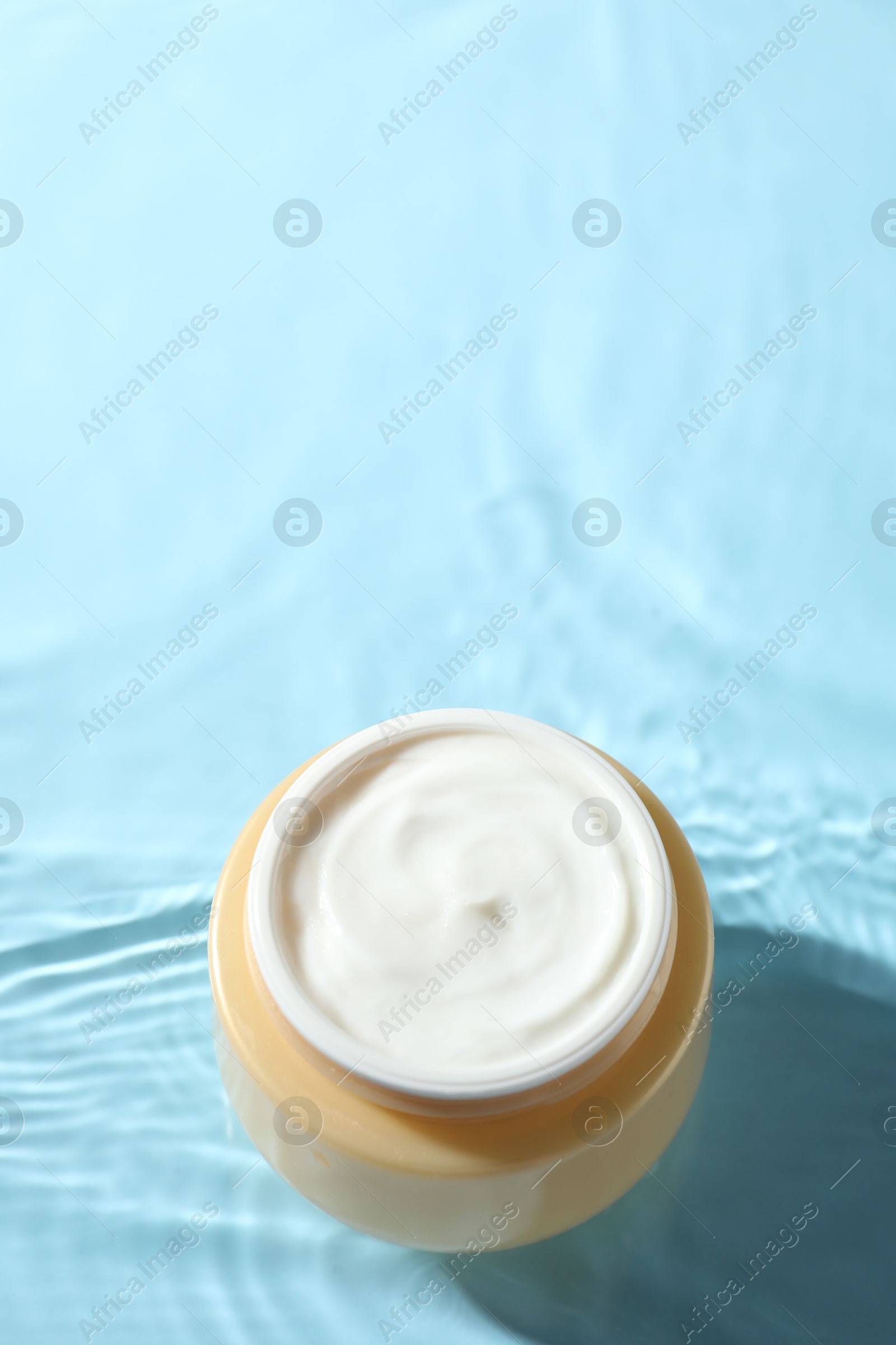 Photo of Jar with face cream in water on light blue background, above view