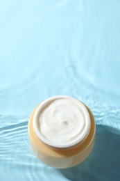 Jar with face cream in water on light blue background, above view