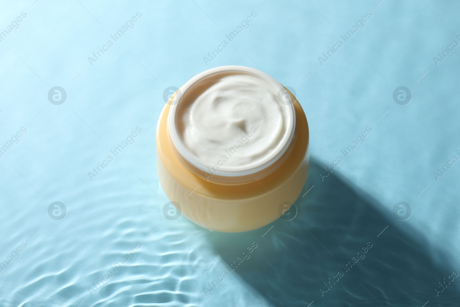 Photo of Jar with face cream in water on light blue background