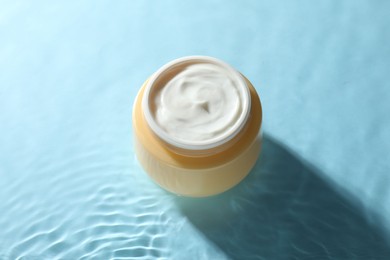 Jar with face cream in water on light blue background