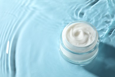 Photo of Jar with face cream in water on light blue background, space for text