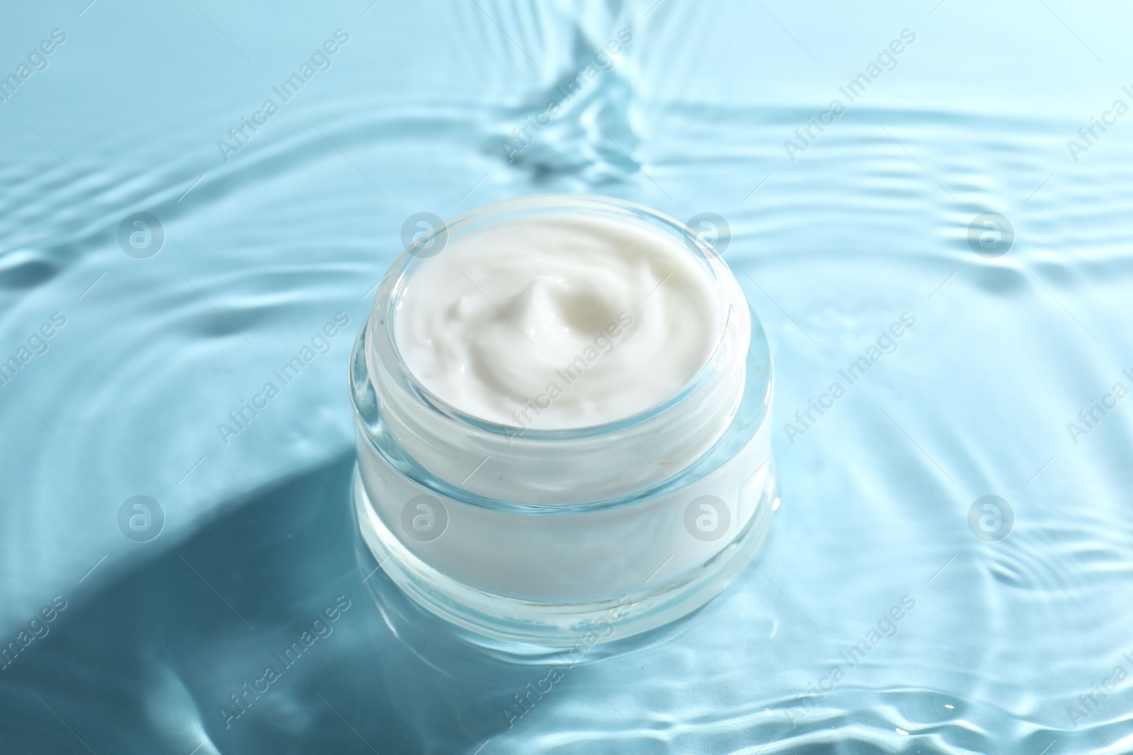 Photo of Jar with face cream in water on light blue background