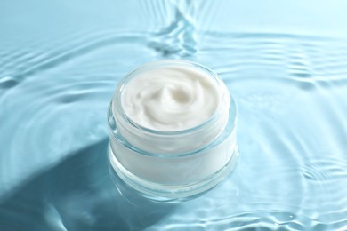 Jar with face cream in water on light blue background