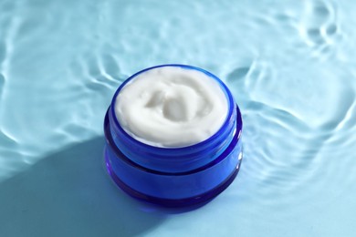 Photo of Jar with face cream in water on light blue background