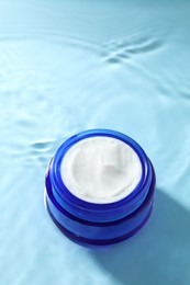 Jar with face cream in water on light blue background, above view