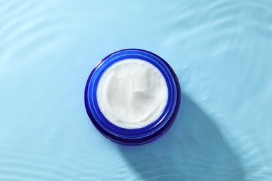 Jar with face cream in water on light blue background, top view