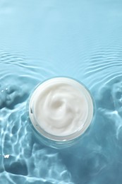 Jar with face cream in water on light blue background, top view