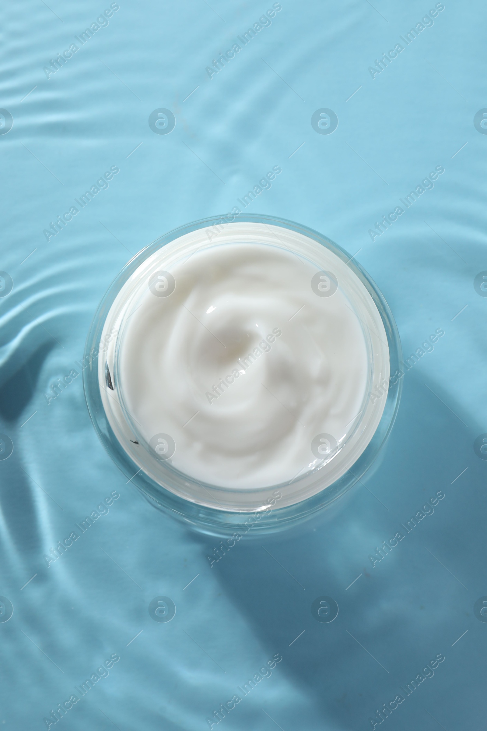 Photo of Jar with face cream in water on light blue background, top view