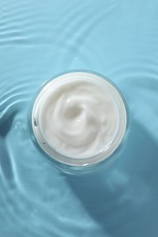 Jar with face cream in water on light blue background, top view