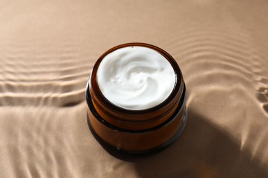 Photo of Jar with face cream in water on beige background