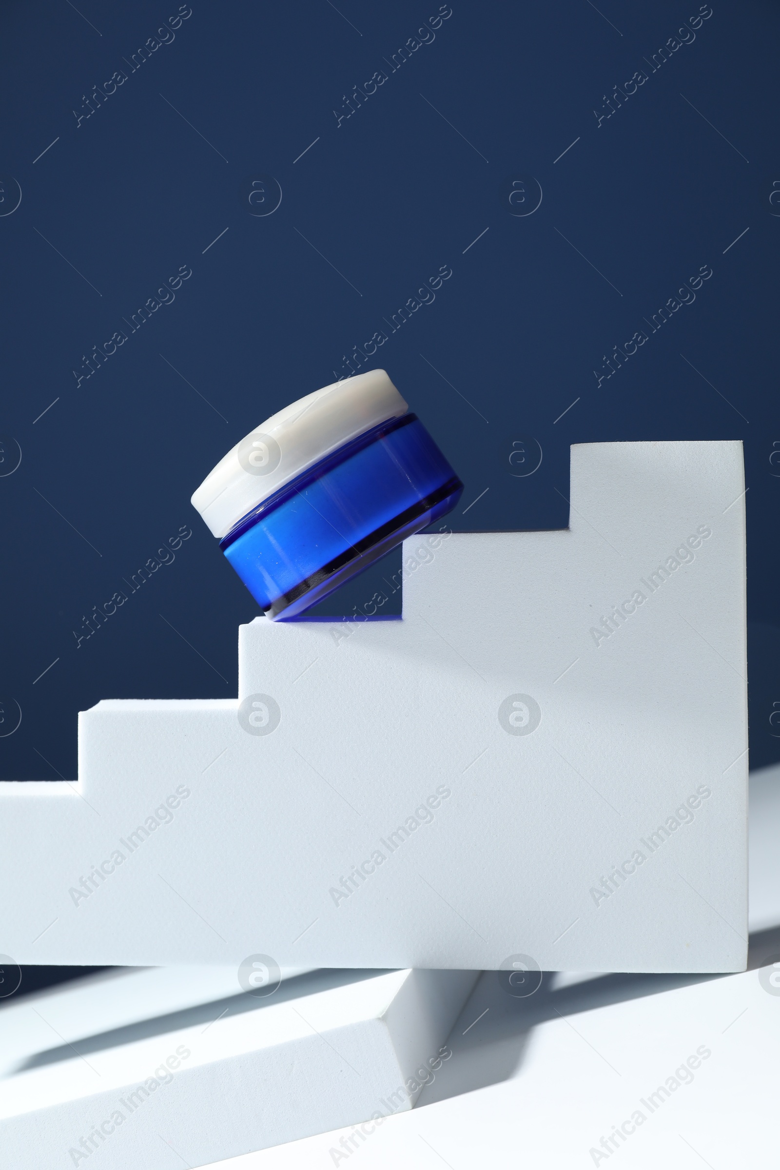 Photo of Stylish presentation of face cream in jar against blue background