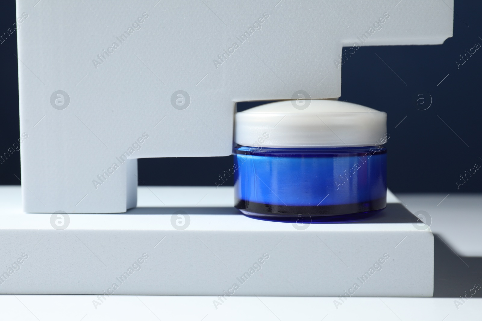 Photo of Stylish presentation of face cream in jar against blue background