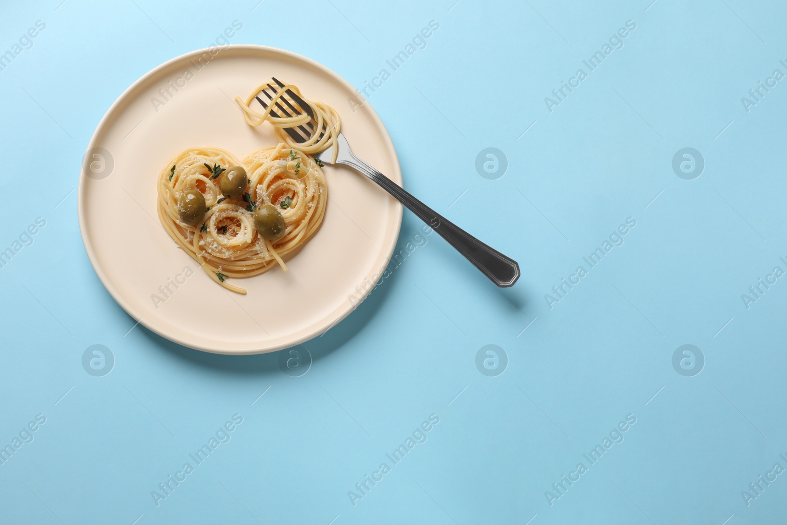 Photo of Heart made of tasty spaghetti, fork, olives and cheese on light blue background, top view. Space for text