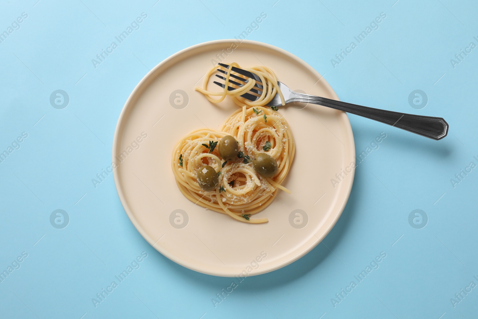 Photo of Heart made of tasty spaghetti, fork, olives and cheese on light blue background, top view