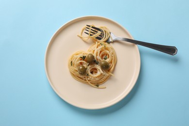 Heart made of tasty spaghetti, fork, olives and cheese on light blue background, top view