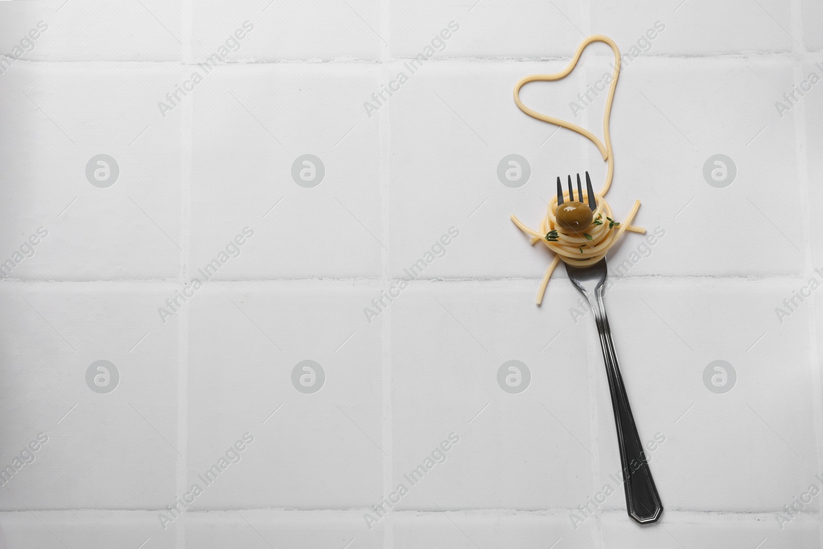 Photo of Heart made of tasty spaghetti, fork and olive on white tiled table, top view. Space for text