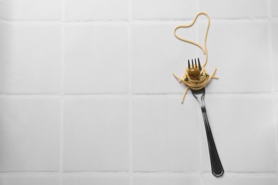 Photo of Heart made of tasty spaghetti, fork and olive on white tiled table, top view. Space for text