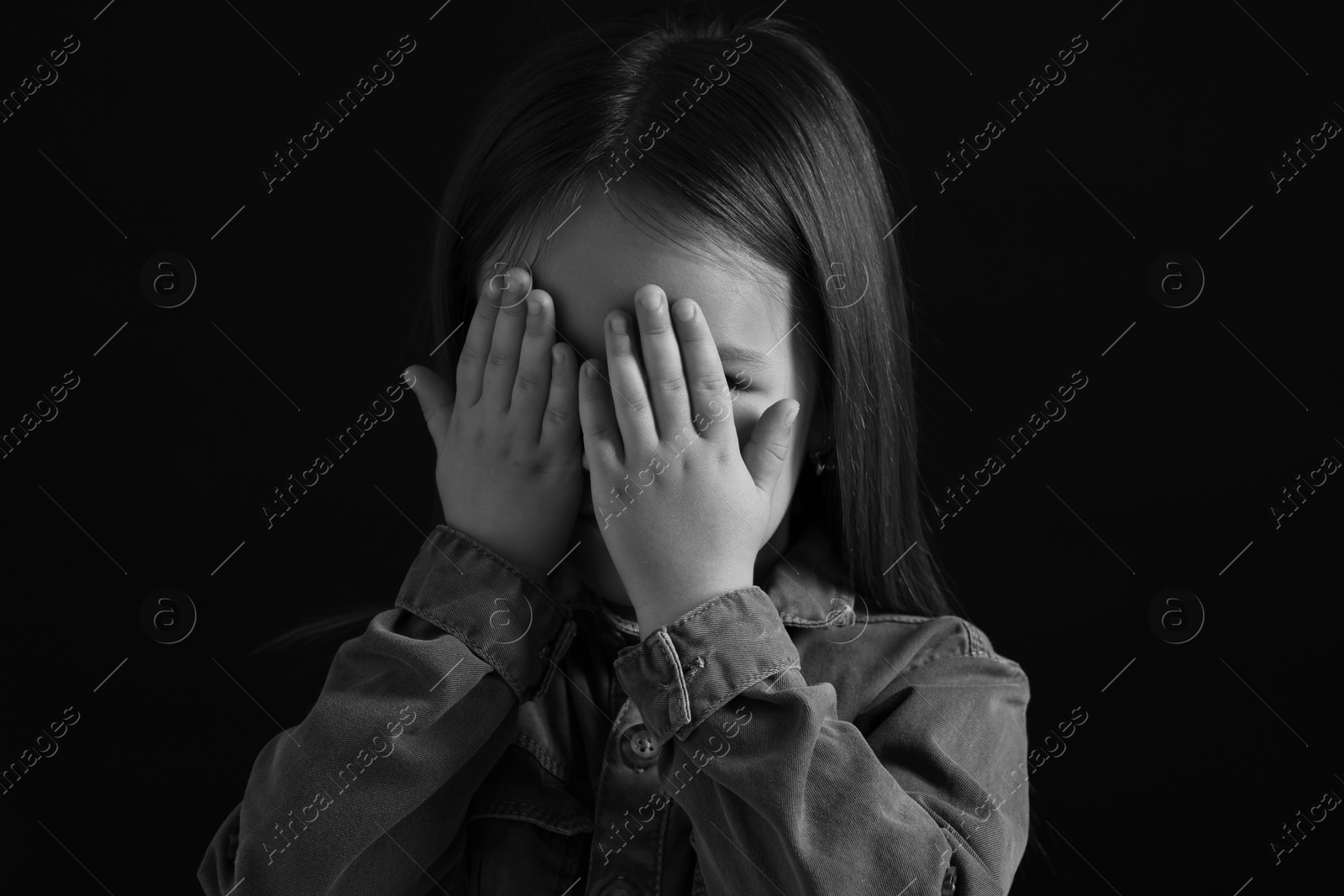 Photo of Girl covering face with hands on dark background, closeup. Black and white effect