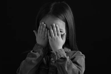 Girl covering face with hands on dark background, closeup. Black and white effect