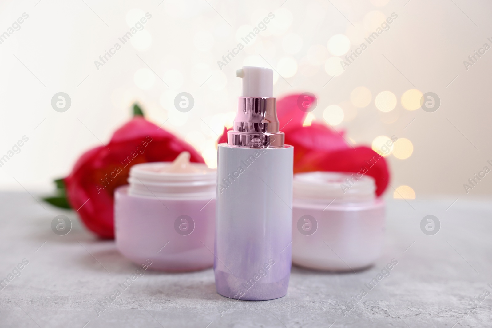 Photo of Set of different cosmetic products and peony flower on gray table against light background with blurred lights, closeup